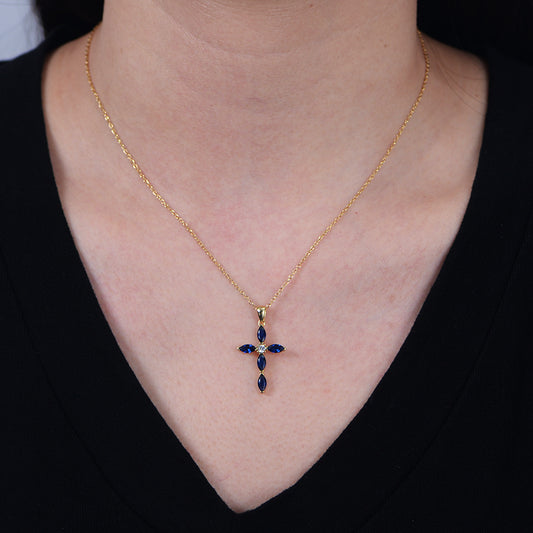 Gold cross necklace with blue stones worn by a woman with a black top