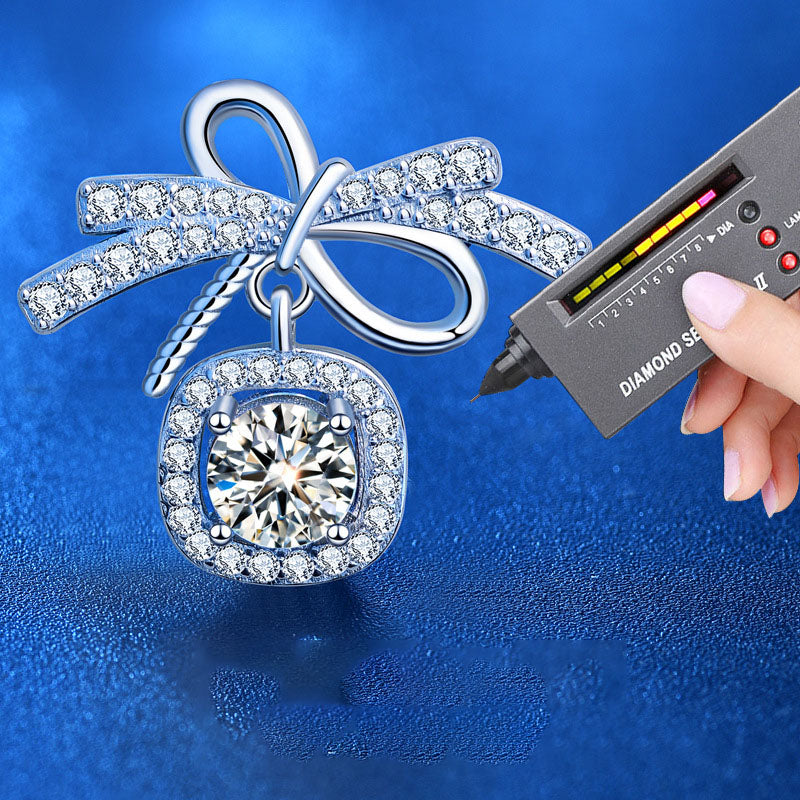 Close-up of bow stud earring with 0.5-carat moissanite and AAA CZ halo, shown with a diamond tester on blue.