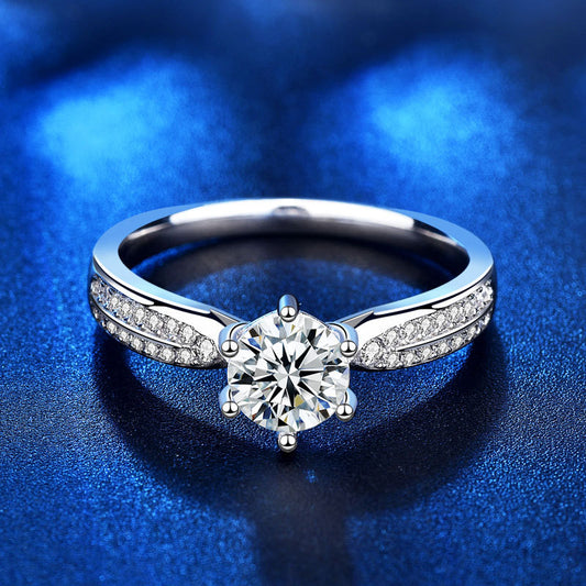 Frontal view of 1 ct round moissanite six-prong ring with pavé CZ-lined band on blue backdrop