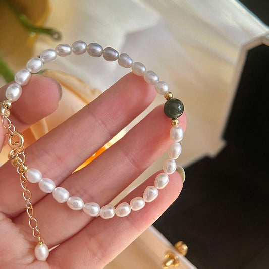 Close-up of dainty shell pearl bracelet with a green jade bead and gold chain