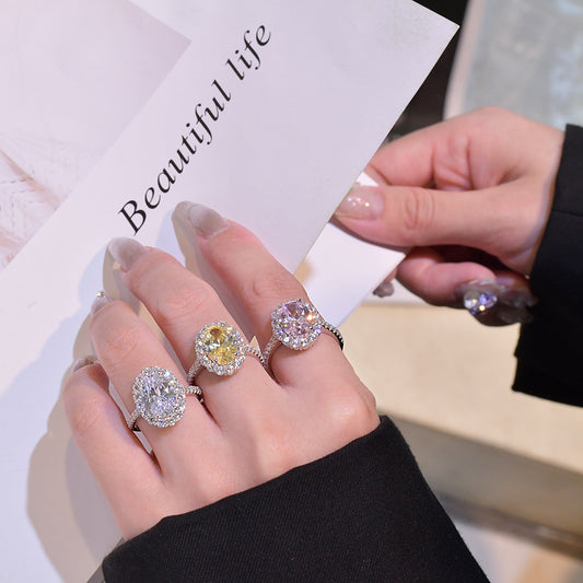 Hand wearing three oval halo CZ rings—white, yellow, and pink centers—for size and sparkle reference.