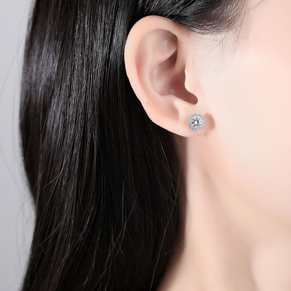 Round halo moissanite stud earring worn on ear for size reference.