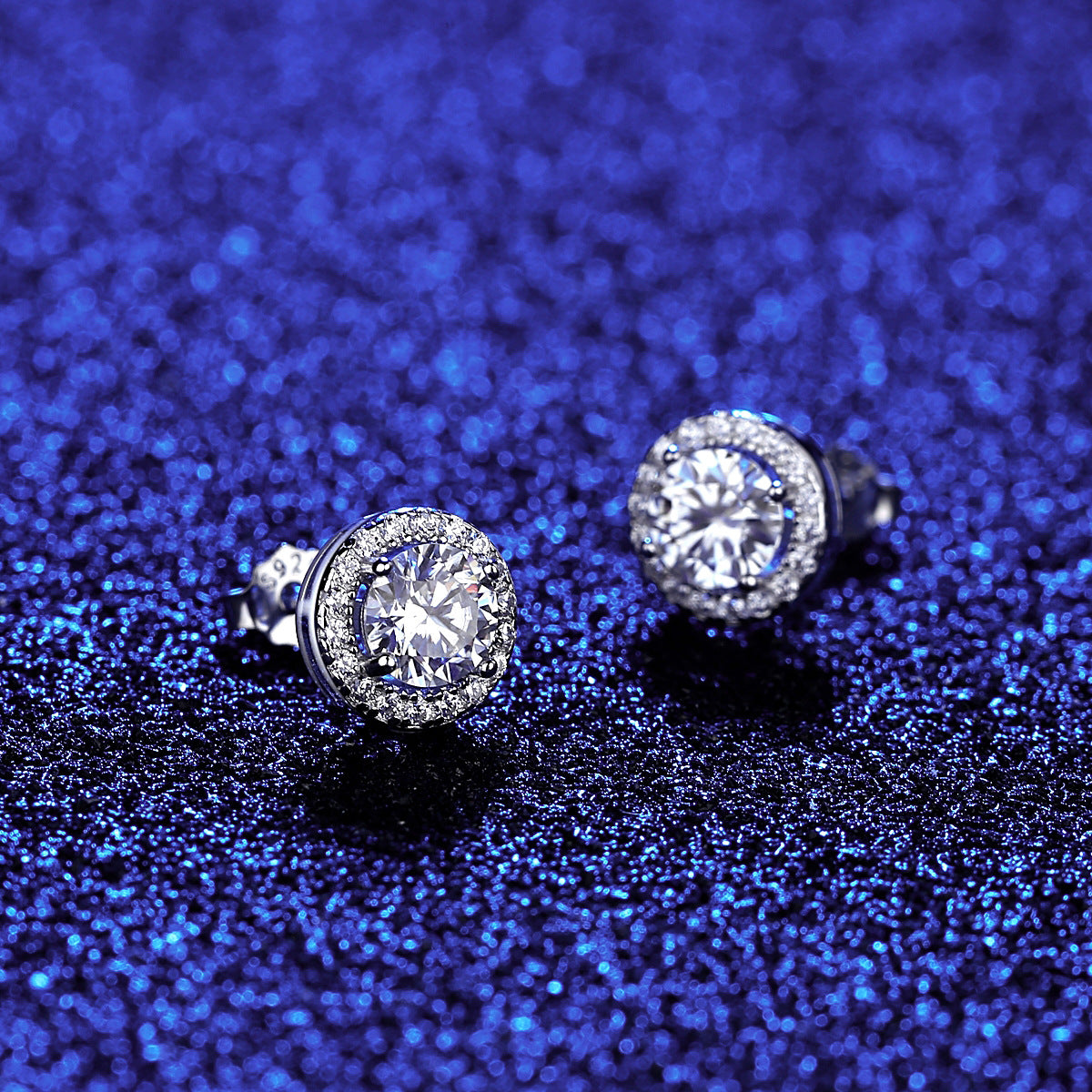 Blue background angled view of round halo moissanite studs showing raised halo setting.