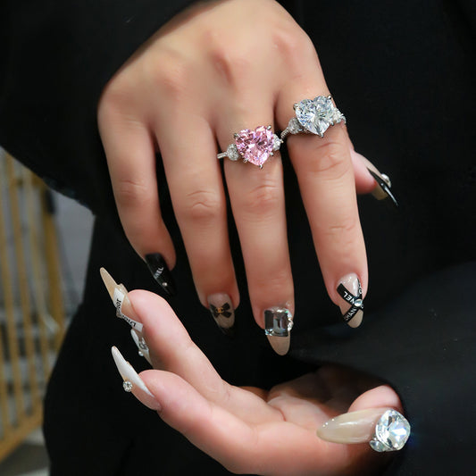 Model wearing pink and white 12mm heart-cut CZ rings in rhodium-plated 925 silver with micro-set accents.