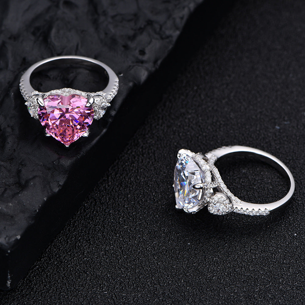 Pink and white 12mm heart-cut CZ rings in rhodium-plated 925 silver with micro-set accents, displayed on black background.