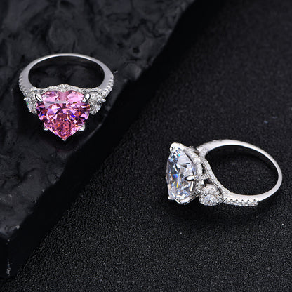 Pink and white 12mm heart-cut CZ rings in rhodium-plated 925 silver with micro-set accents, displayed on black background.