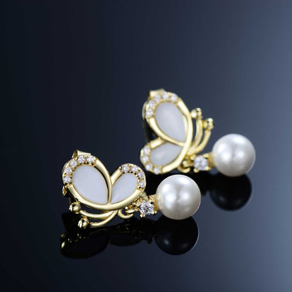 White enamel butterfly pearl dangle earrings with CZ accents on a reflective black background.