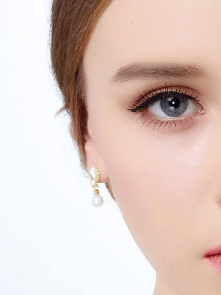 Front close-up of model wearing white enamel butterfly pearl dangle earring in 18K gold-plated 925 silver with CZ accents.