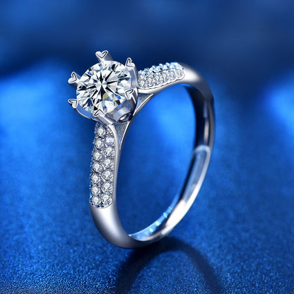 Angled view of 1 carat round moissanite ring with six prongs and pavé CZ shoulders in sterling silver.