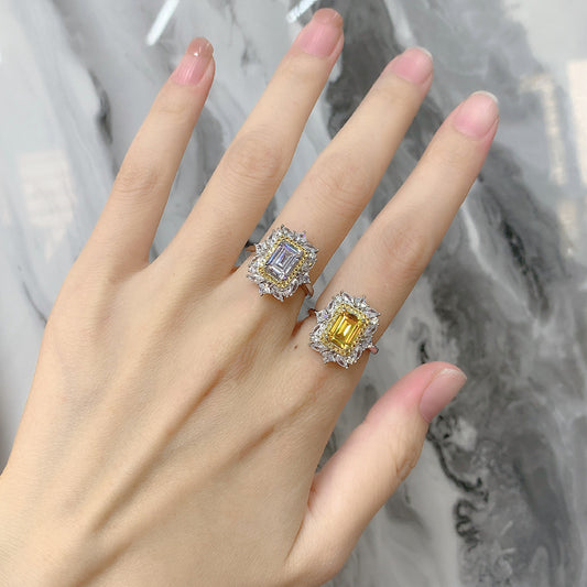 Hand wearing two baguette-cut CZ halo rings, one yellow center and one white center.