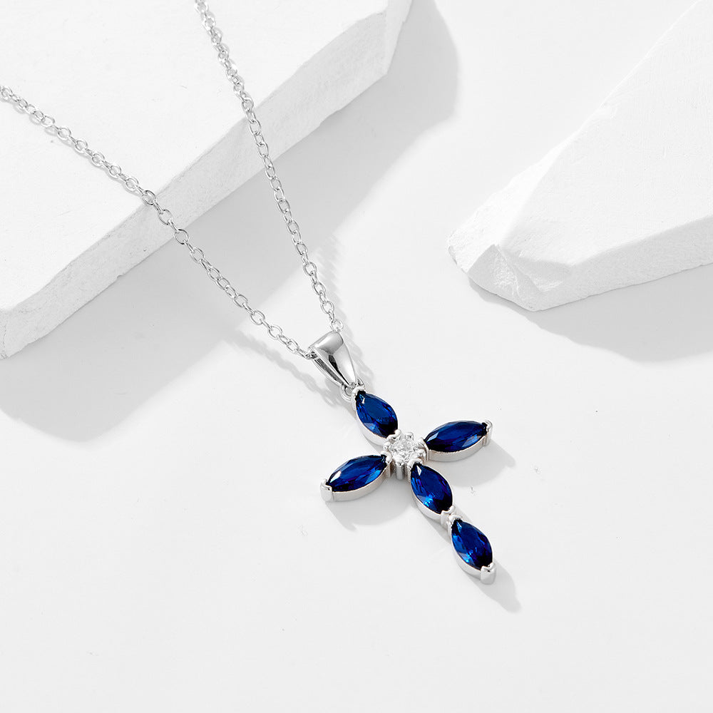 Silver-tone cross necklace with vivid blue stones displayed on a minimal white setting