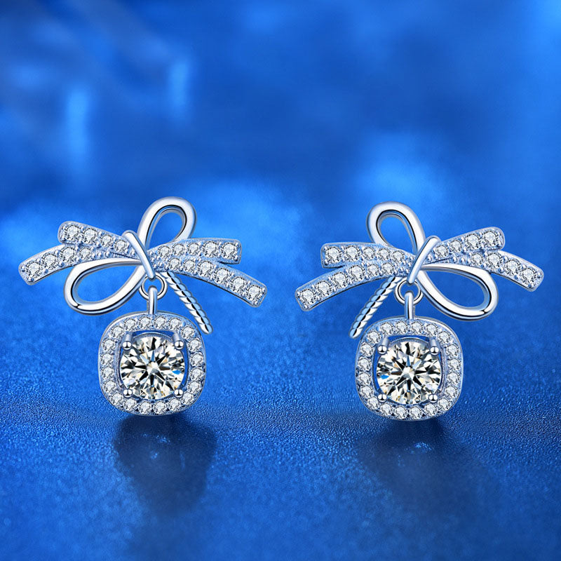 Bow 0.5-carat moissanite stud earrings with AAA CZ halo in rhodium-plated sterling silver, front view on blue background.