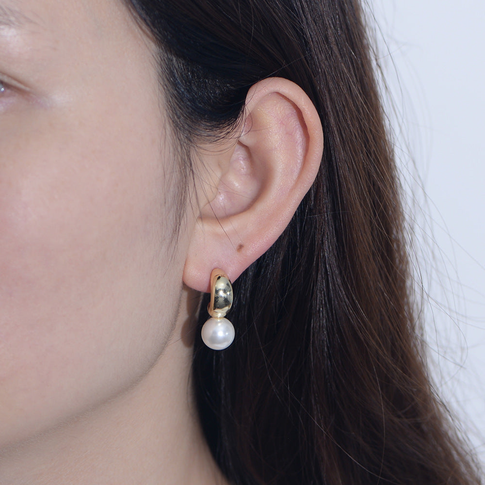 Model wearing gold-finish C-hoop created pearl dangle earring.