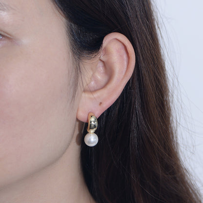 Model wearing gold-finish C-hoop created pearl dangle earring.