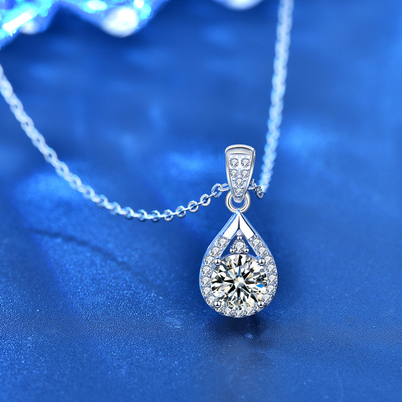 Teardrop moissanite pendant with CZ accents shown on chain against a deep blue backdrop