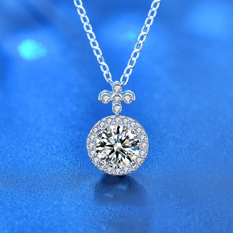 Close-up of moissanite halo pendant with fleur-de-lis bail on a sterling silver chain, blue background.