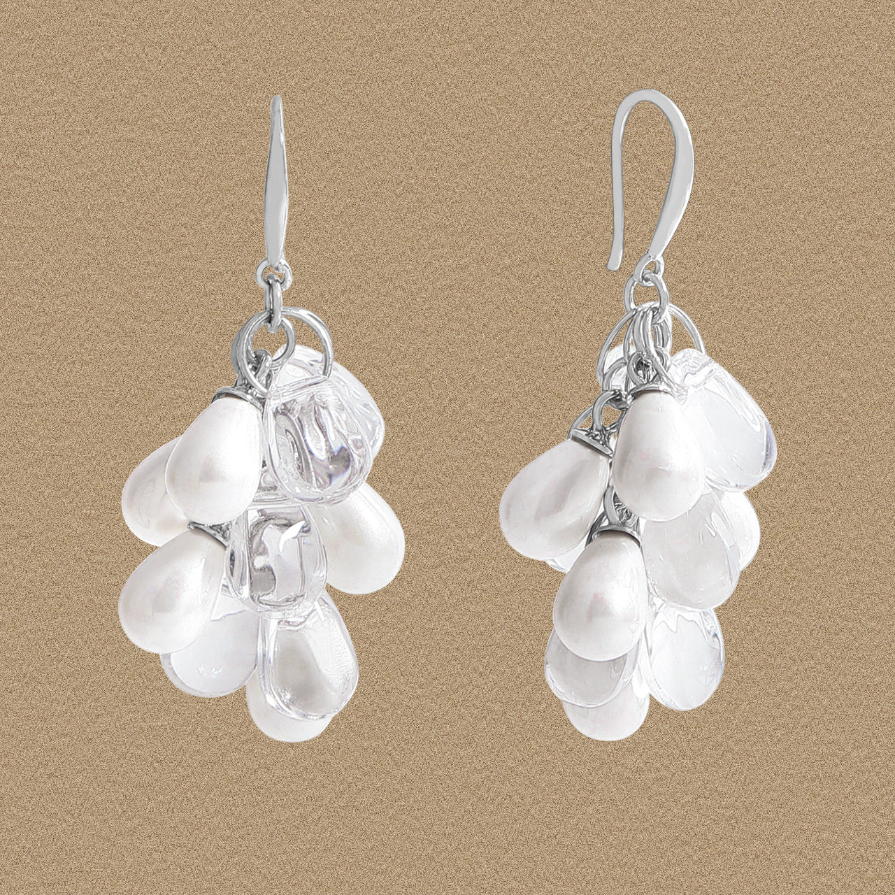 Front view of grape-cluster dangle earrings with white shell pearls and clear droplets in 925 silver on a beige background.