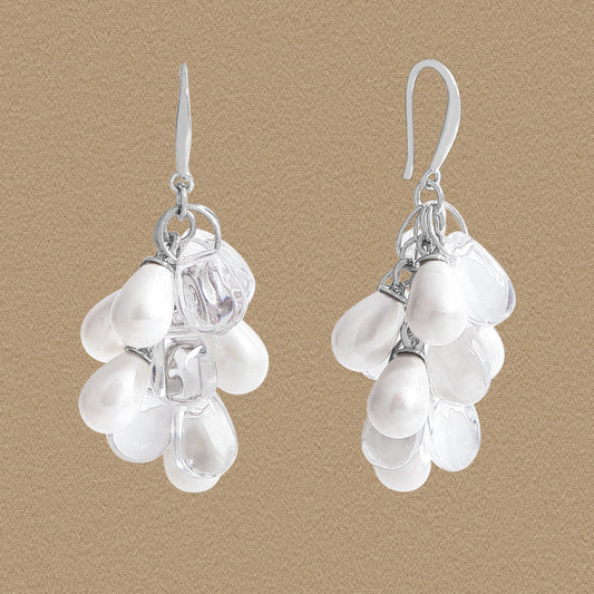 Front view of grape-cluster dangle earrings with white shell pearls and clear droplets in 925 silver on a beige background.