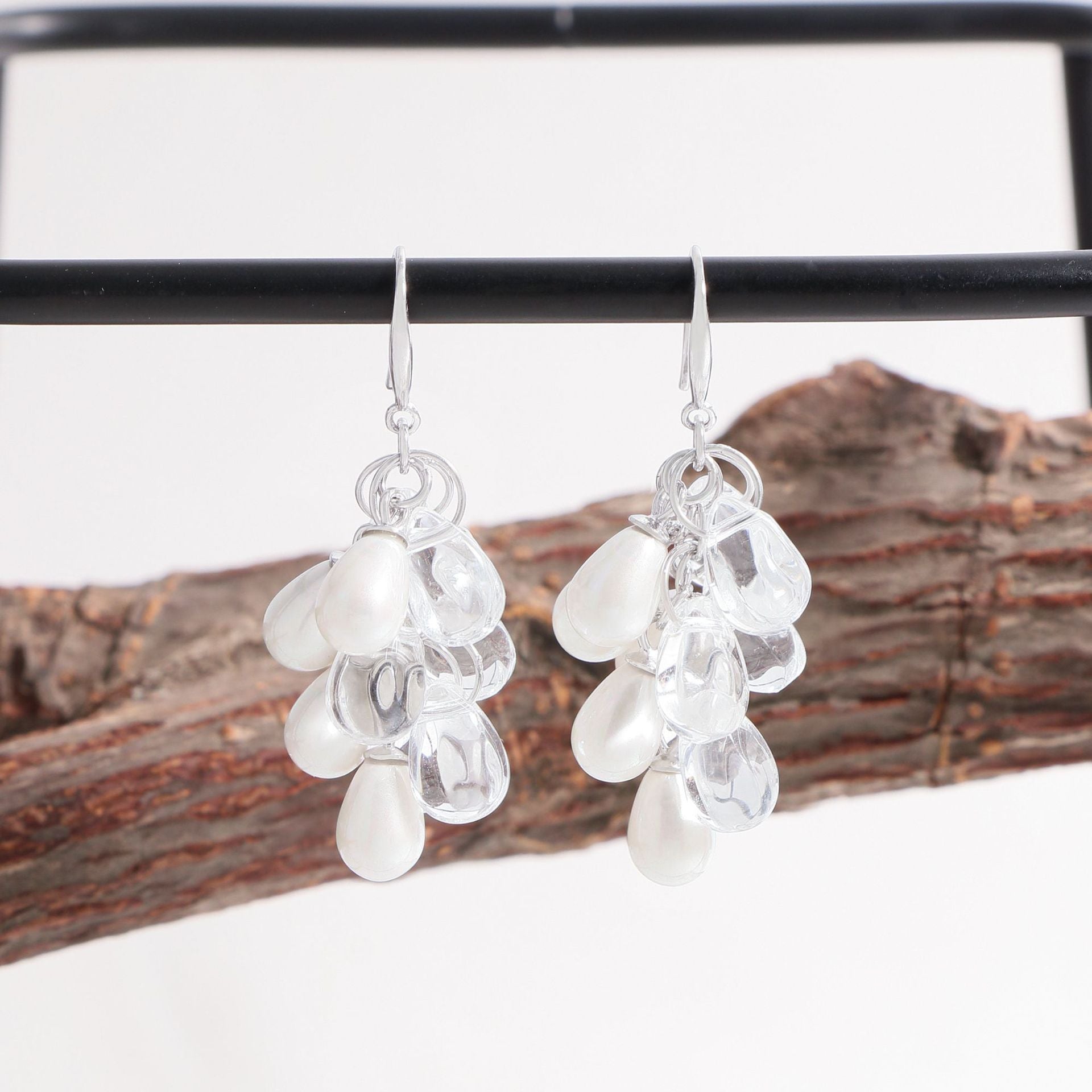 Pair of shell-pearl grape-cluster dangle earrings hanging on a display bar, 925 sterling silver with clear droplet accents.