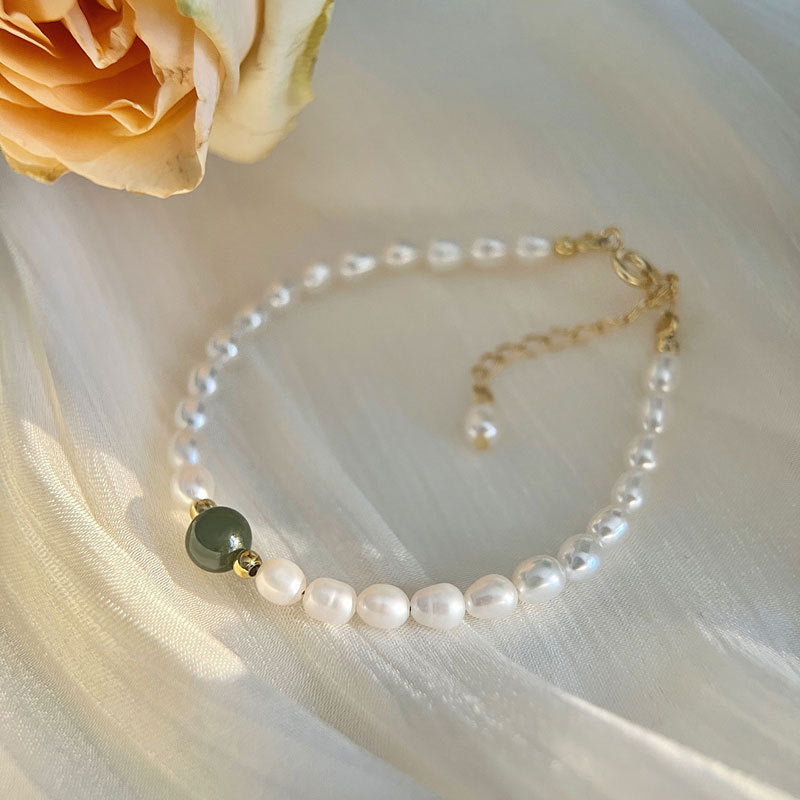 Jade bead and shell pearl bracelet with gold accents on soft white fabric