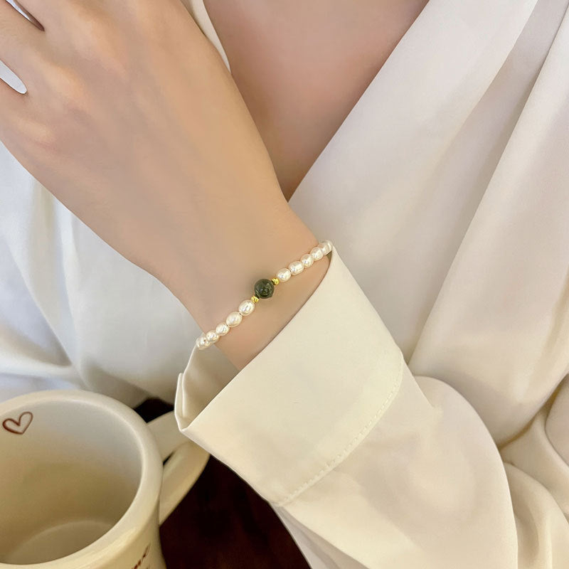 Woman wearing jade and shell pearl bracelet with white blouse.