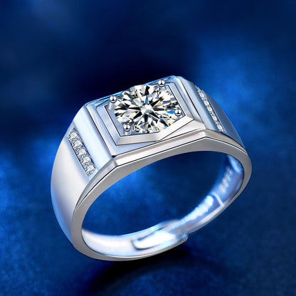 Angled view of men’s round-cut moissanite signet ring, four-prong set, geometric bezel, in 925 silver on blue.