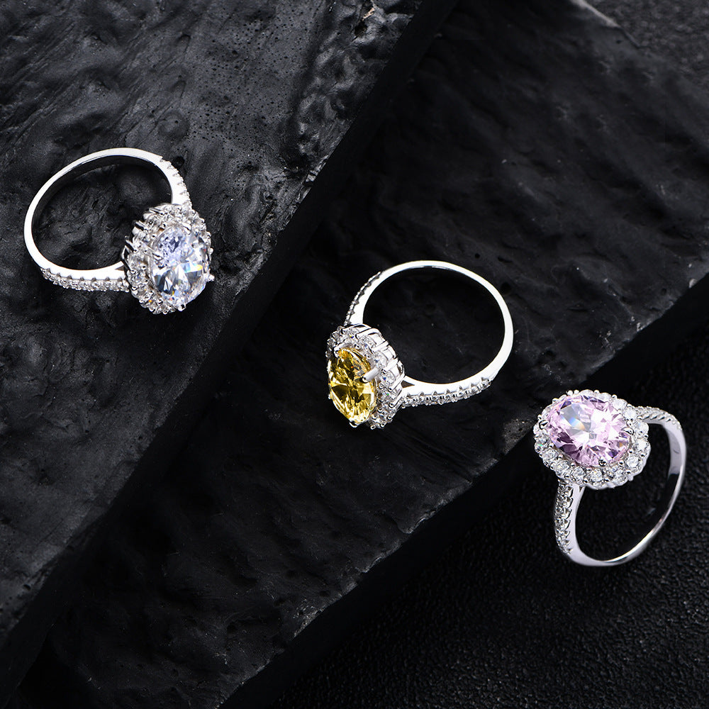 Three oval halo CZ rings in sterling silver—white, yellow, and pink centers—on black stone background.