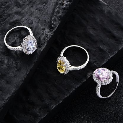 Three oval halo CZ rings in sterling silver—white, yellow, and pink centers—on black stone background.