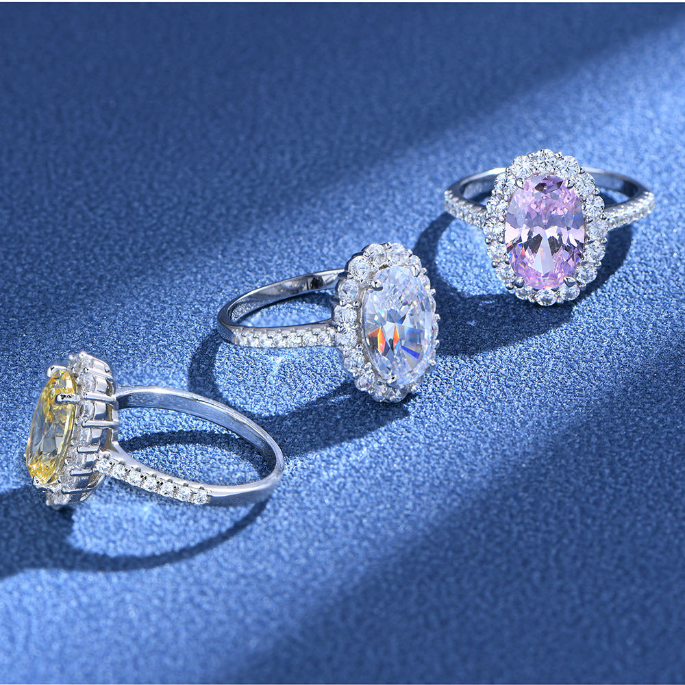 Oval halo CZ rings in sterling silver with white, pink, and yellow centers shown on a blue textured surface.