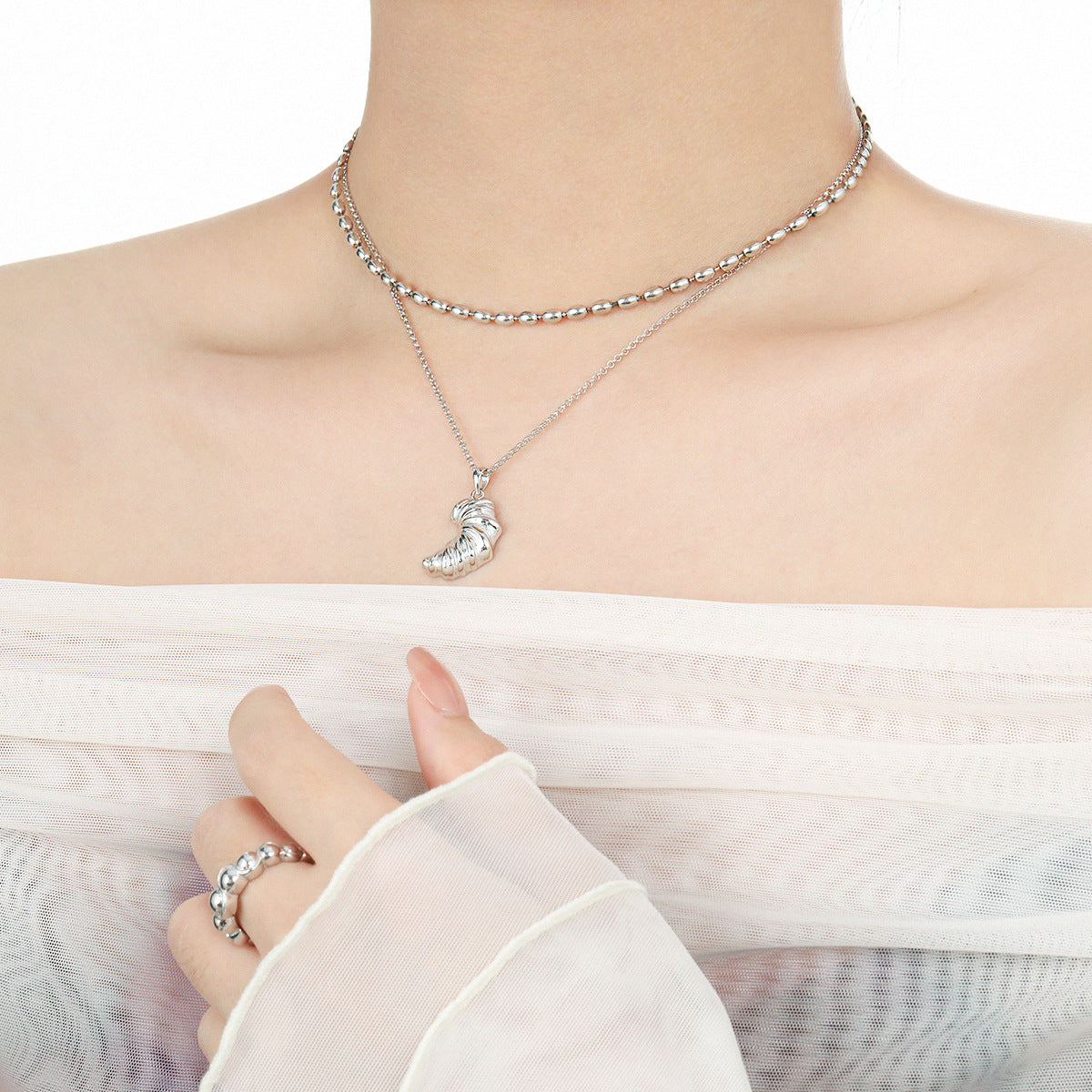 Model layering a sterling silver croissant pendant with a beaded choker