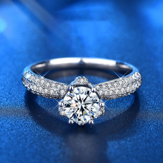 Front view of crown-set moissanite ring with pavé CZ shoulders in rhodium-plated 925 silver on blue background.