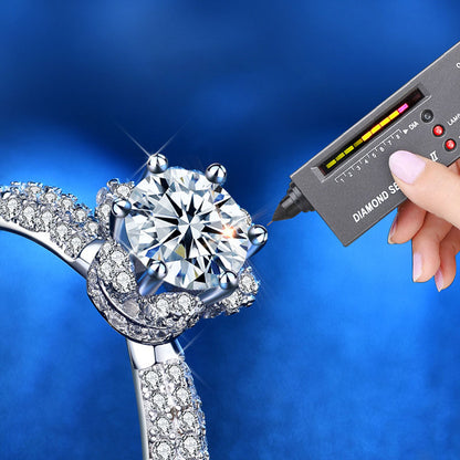 A diamond tester points to 1 ct moissanite stone set in crown design with pavé-set CZ on the ring shoulders.