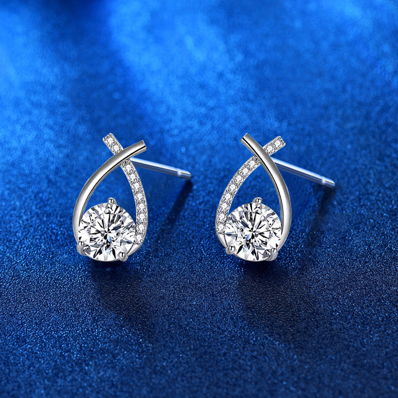 Angled view of ribbon-twist moissanite stud earrings in rhodium-plated sterling silver, pavé CZ band, blue background