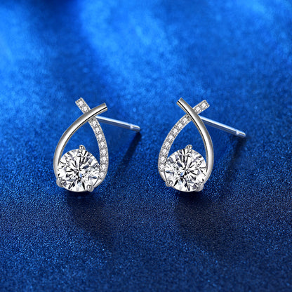 Angled view of ribbon-twist moissanite stud earrings in rhodium-plated sterling silver, pavé CZ band, blue background