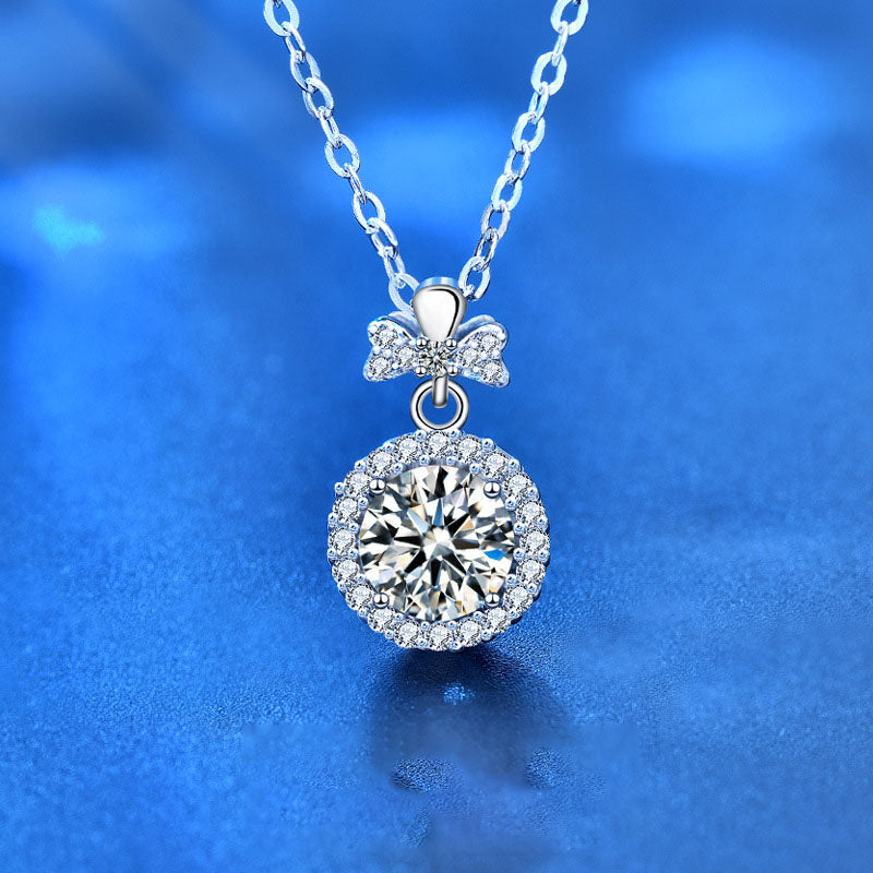 Close-up of sterling silver perfume bottle pendant necklace featuring round moissanite and bow accent on blue background